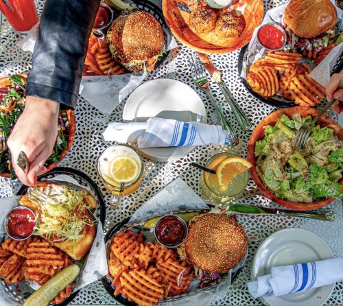 A vibrant spread of burgers, salads, and sweet potato fries on a table, with drinks and utensils ready for a meal.