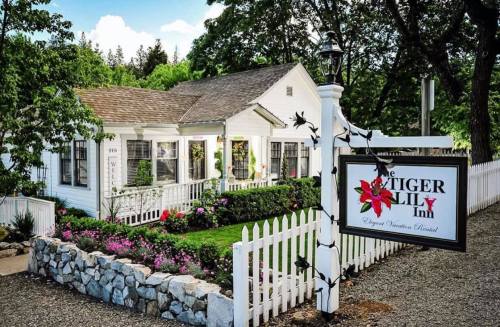 A charming white inn with a flower garden, surrounded by a picket fence and a sign reading "The Tiger Lily Inn."