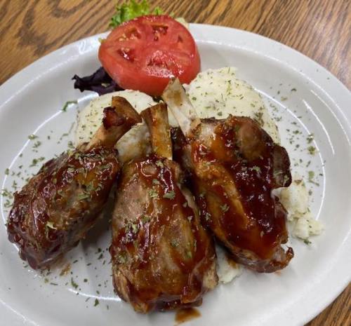 Three glazed meat chops served with mashed potatoes and a slice of tomato on a white plate.