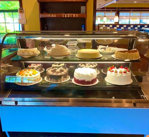 A display case filled with various cakes, including chocolate, fruit-topped, and cream cakes, in a cozy restaurant setting.