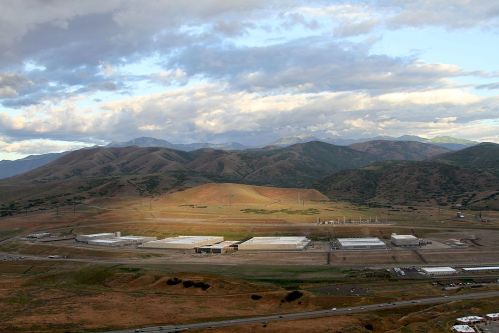 Aerial view of industrial buildings in a valley surrounded by mountains under a partly cloudy sky.