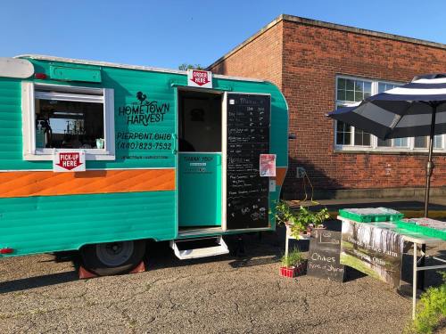 A colorful food truck with a menu displayed outside, surrounded by plants and a table for orders.