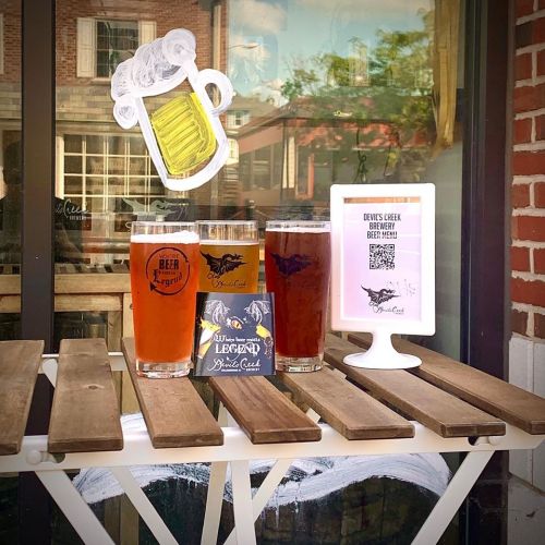 Three glasses of beer on a wooden table, with a sign for Devil's Creek Brewery and a QR code nearby.