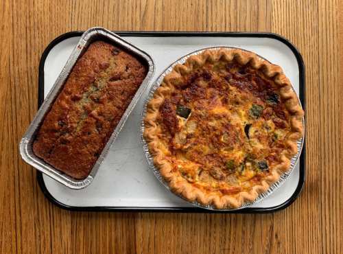 A wooden table holds a savory pie and a loaf of bread on a tray, showcasing their golden crusts and rich textures.