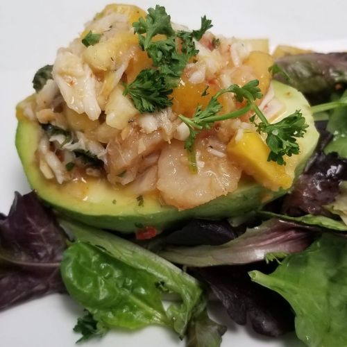 A halved avocado topped with a seafood salad and garnished with parsley, served on a bed of mixed greens.