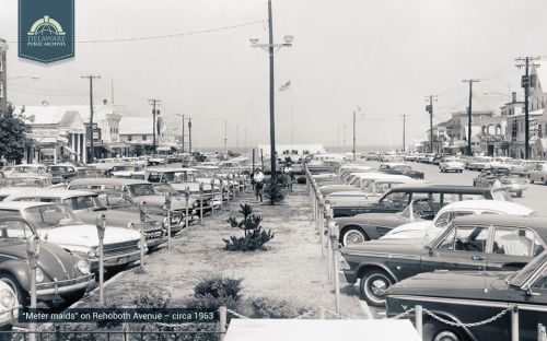 Black and white photo of Rehoboth Avenue in 1963, featuring parked cars and a view of the beach in the distance.