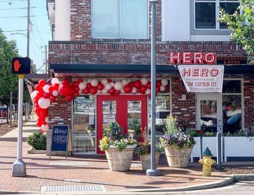 A storefront with red and white balloons, a sign reading "HERO" and "NOW OPEN," and flower pots on the sidewalk.