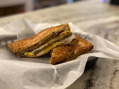 A toasted sandwich with layers of egg and sausage, served on parchment paper in a black basket.