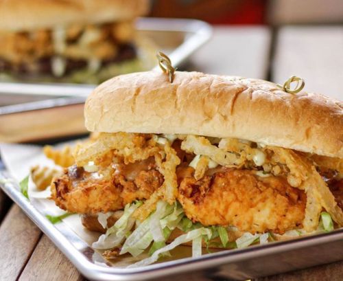A crispy fried chicken sandwich with lettuce, topped with crispy onions, served on a soft bun.
