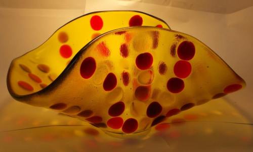 A vibrant yellow glass bowl with red polka dots, featuring a wavy, sculptural design.