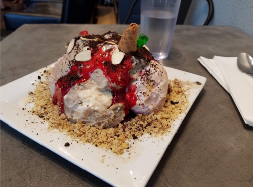A large dessert with scoops of ice cream, chocolate syrup, nuts, and a cherry, served on a white plate.