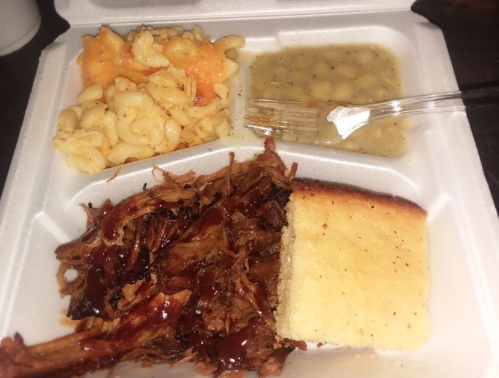 A takeout container with pulled pork in barbecue sauce, macaroni and cheese, potato salad, and a piece of cornbread.