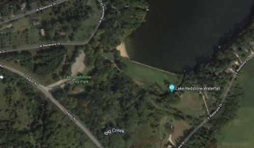 Aerial view of Lake Redstone County Park, featuring a waterfall, creek, and surrounding greenery.