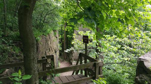 A wooden pathway leads through lush greenery and rocky cliffs, with a sign indicating the trail ahead.
