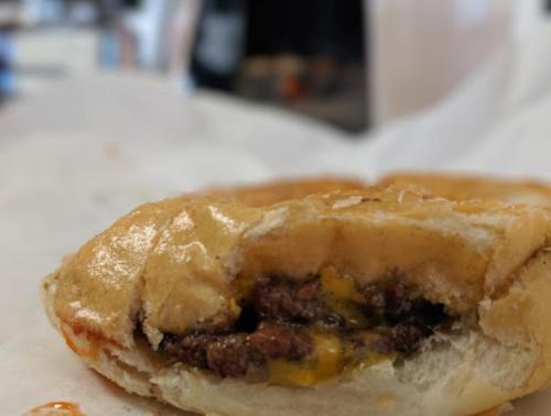 Close-up of a partially eaten cheeseburger with melted cheese and a soft bun, set against a blurred background.
