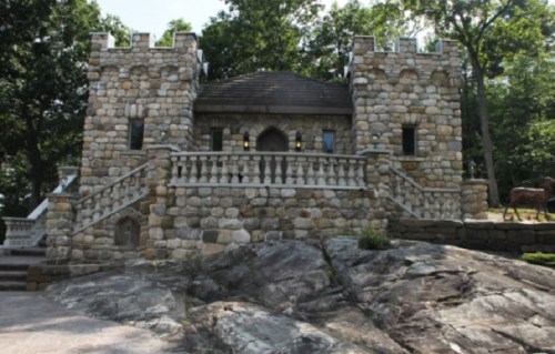A stone castle with turrets, surrounded by trees and built on a rocky landscape.