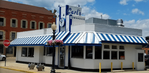 A white building with blue and white striped awning, featuring a sign that reads "Carl's Townhouse" and flower planters.