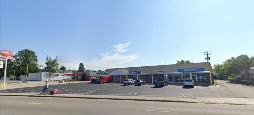 A sunny street view of a small shopping plaza with several storefronts and parked cars.