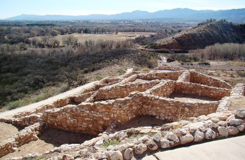 Ancient stone ruins on a hillside, overlooking a valley with mountains in the distance under a clear blue sky.