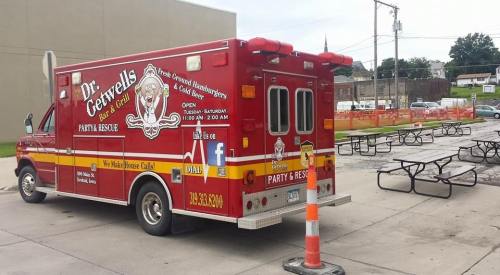 A red food truck with "Dr. Getwell's" branding parked near picnic tables, offering fresh burgers and hot dogs.