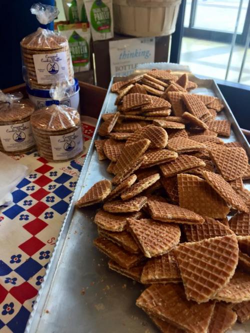 A tray of stacked waffle cookies on a table, with packaged cookies in the background.