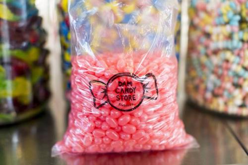 A clear bag filled with pink jelly beans, labeled "Dan Candy Store" with colorful candies in the background.