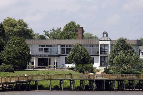 A view of the Decoy Museum, surrounded by trees, with a wooden pier extending into the water.