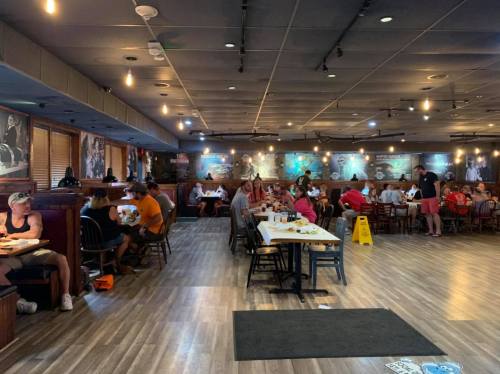 A busy restaurant interior with diners at tables, wooden decor, and wall art, creating a lively atmosphere.
