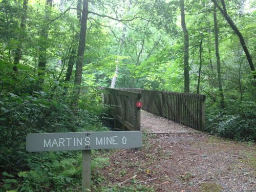 A wooden bridge leads into a lush green forest, with a sign reading "Martin's Mine" in the foreground.