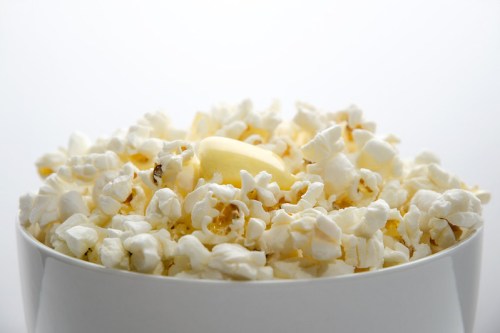 A close-up of a bowl filled with fluffy popcorn, topped with a pat of butter against a light background.