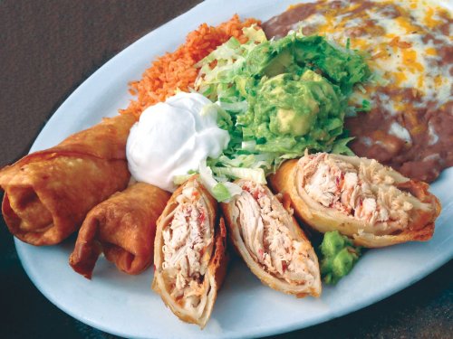 A plate of crispy taquitos filled with chicken, served with rice, refried beans, guacamole, lettuce, and sour cream.