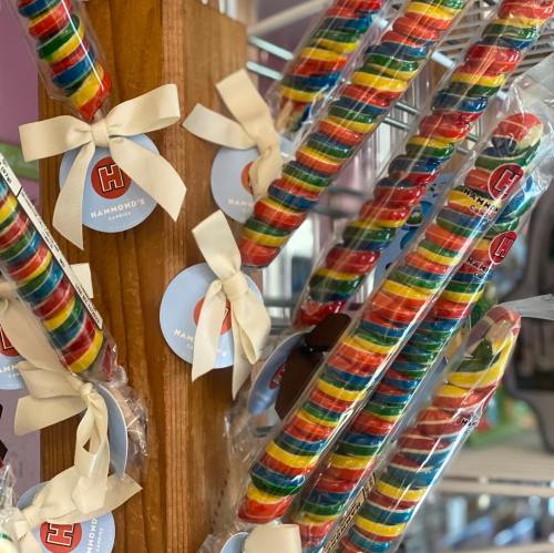 Colorful rainbow lollipops displayed on a wooden stand, each tied with a ribbon and featuring a logo.
