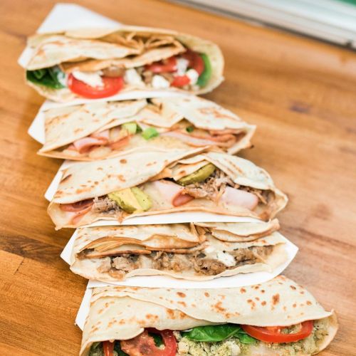 A row of delicious wraps filled with various ingredients like meats, vegetables, and sauces on a wooden surface.