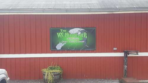 Sign on a red barn wall reading "The W.V. Hellbender: 132 Miles, Over 1300 Curves" with a graphic of a river.