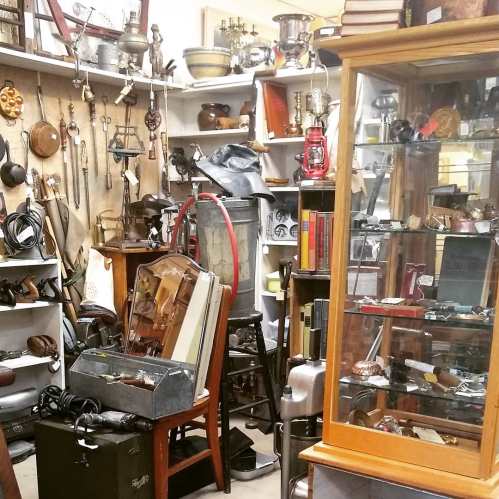 A cluttered antique shop filled with various vintage items, tools, and display cases showcasing collectibles.