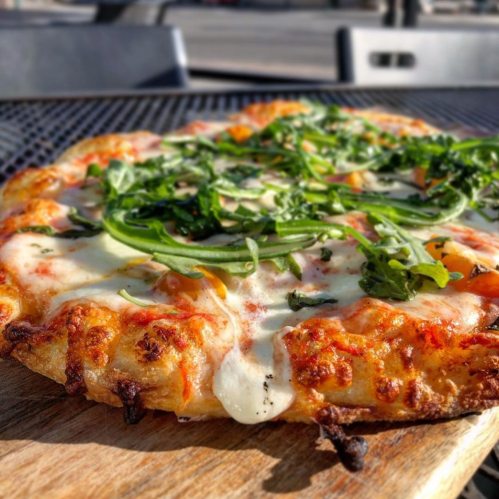 A close-up of a freshly baked pizza topped with melted cheese, fresh greens, and a crispy crust on a wooden board.