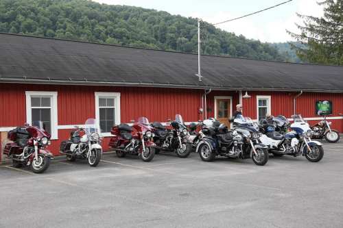 A row of various motorcycles parked in front of a red building with green hills in the background.