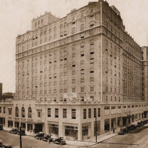Historic hotel building with ornate architecture, surrounded by vintage cars on a city street.