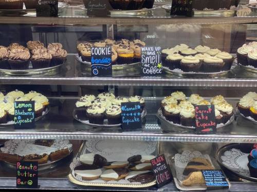 A display case filled with various cupcakes and desserts, each labeled with colorful signs.
