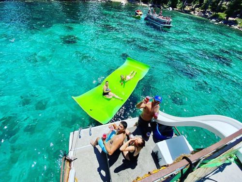A group of people enjoying a sunny day on a boat, with a floating mat in clear turquoise water.