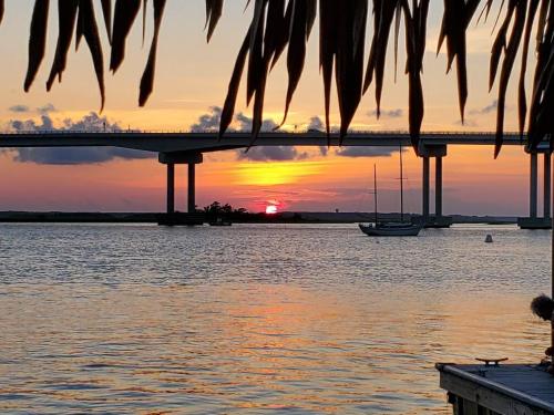 A vibrant sunset over water, with a bridge in the background and a sailboat gently bobbing in the foreground.