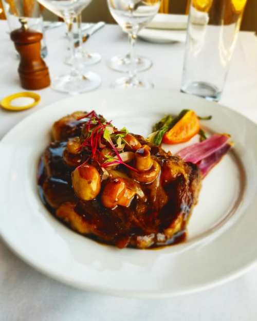A plated dish featuring a juicy steak topped with mushrooms and sauce, garnished with herbs and served with vegetables.