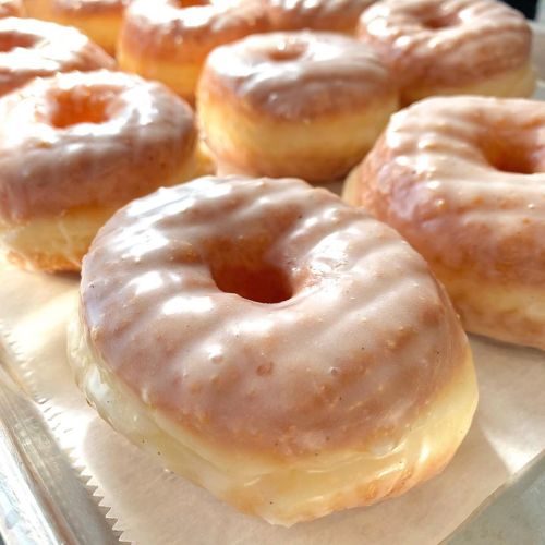 A close-up of glazed donuts arranged on a tray, showcasing their shiny, sugary surface.