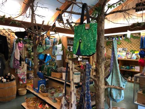 A cozy shop interior with bags and crafts displayed on wooden tables and trees, surrounded by colorful merchandise.