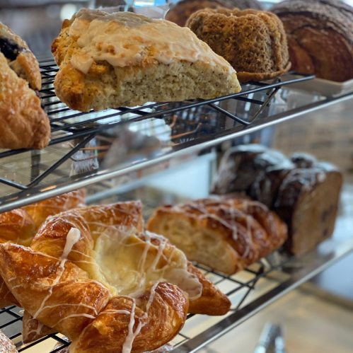 A display of assorted baked goods, including scones, croissants, and loaves of bread, on wire racks.