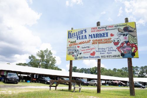Sign for Keller's Flea Market with details about features, parking, and hours, set against a cloudy sky.