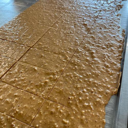 A large, smooth slab of fudge cut into squares, with a glossy, caramel-colored surface.