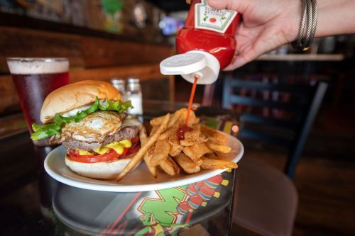 A close-up of a burger with lettuce, tomato, and an egg, served with fries and ketchup, alongside a drink.
