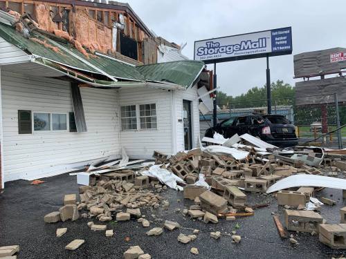 Damaged building with a torn roof, debris scattered on the ground, and a sign for "The Storage Mall" visible.