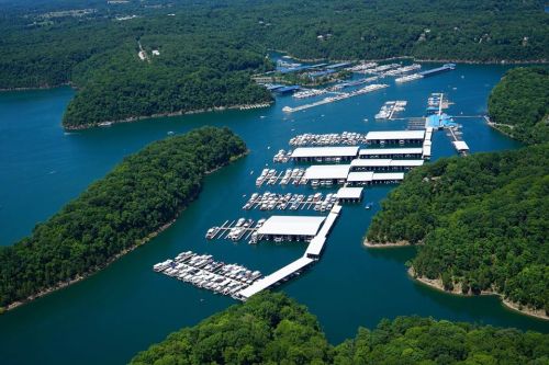 Aerial view of a marina surrounded by lush green hills and blue water, with numerous boats docked.